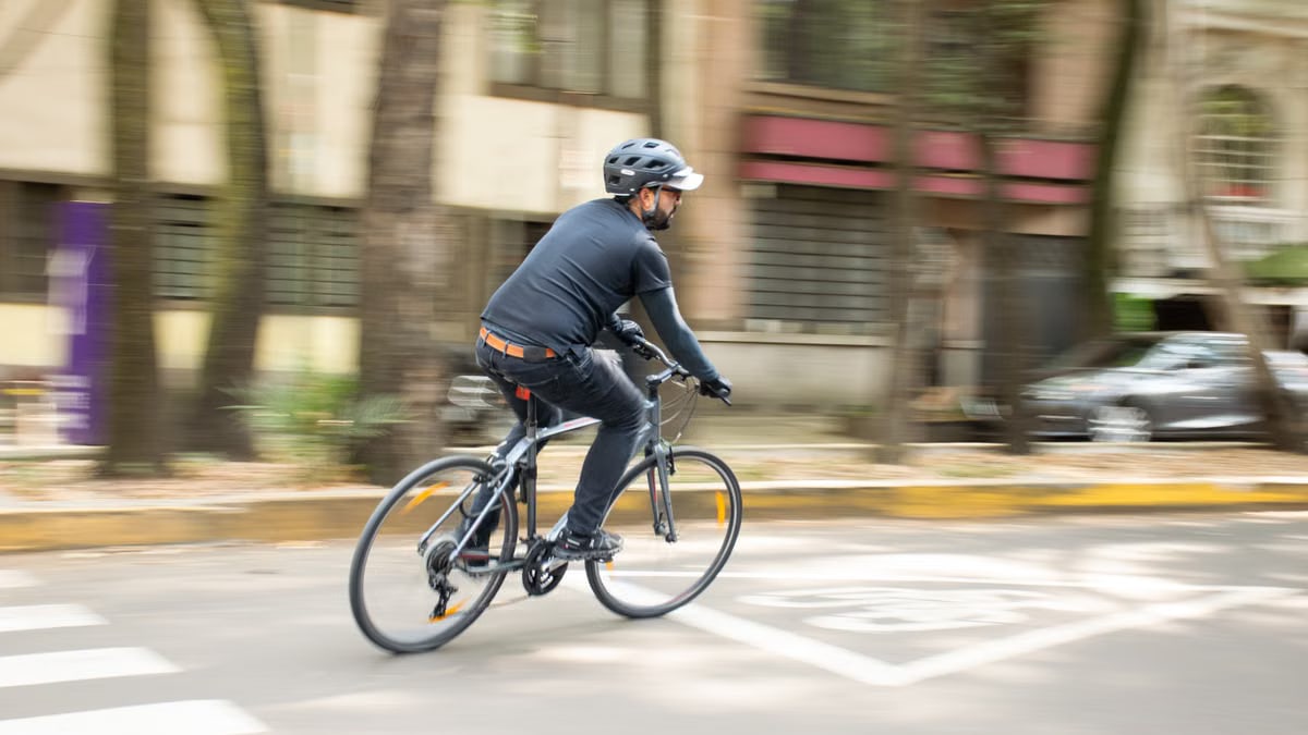 Adult male cycling on city street with helmet, promoting urban mobility.