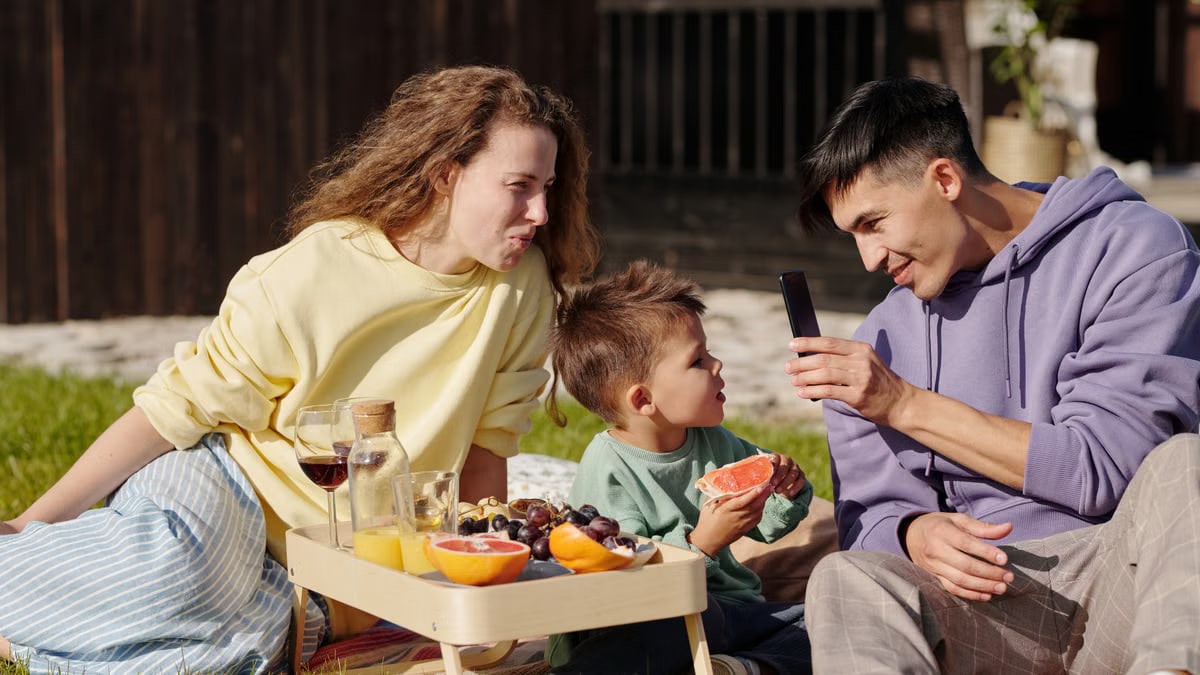 Smiling family having a picnic with fresh fruit on a sunny day, capturing memories.