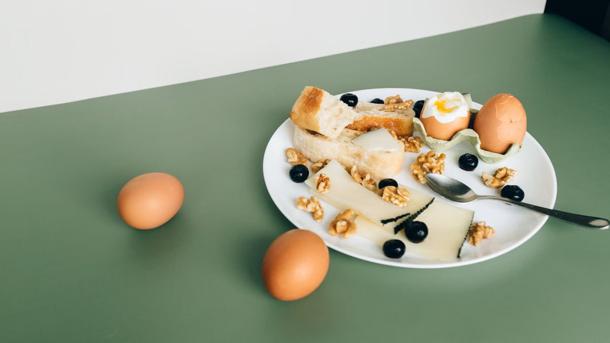 Plate of cheese, boiled eggs, bread, walnuts, and blueberries for a hearty breakfast.